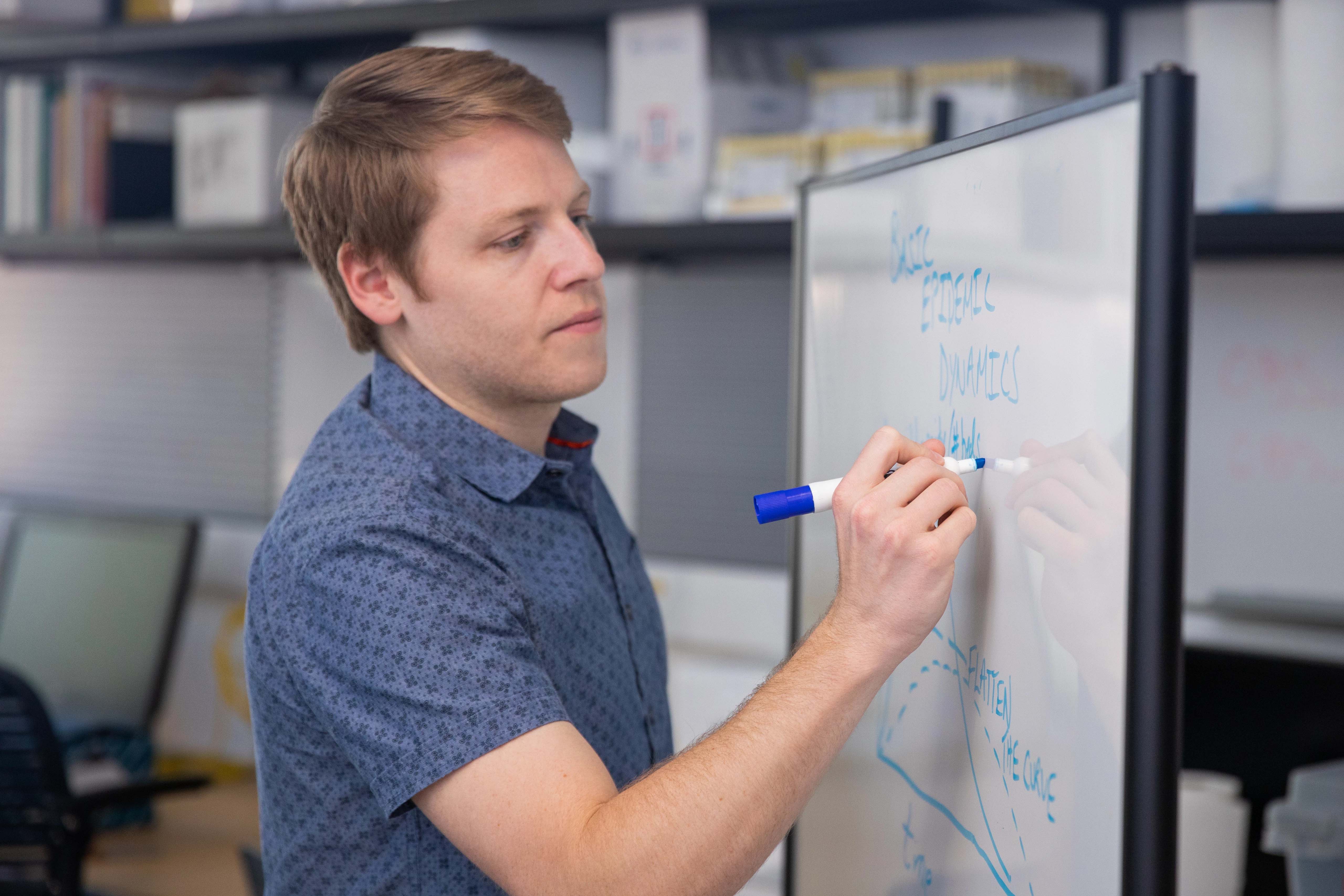 NAU Associate Professor, Joe Mihaljevic, writing on a white board.