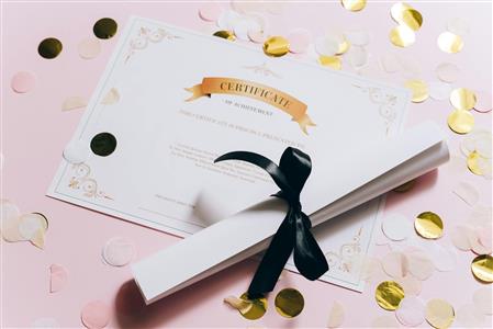 Photo of a diploma on a table with confetti strewn around it, and a second rolled up certificate with a bow wrapped around it.